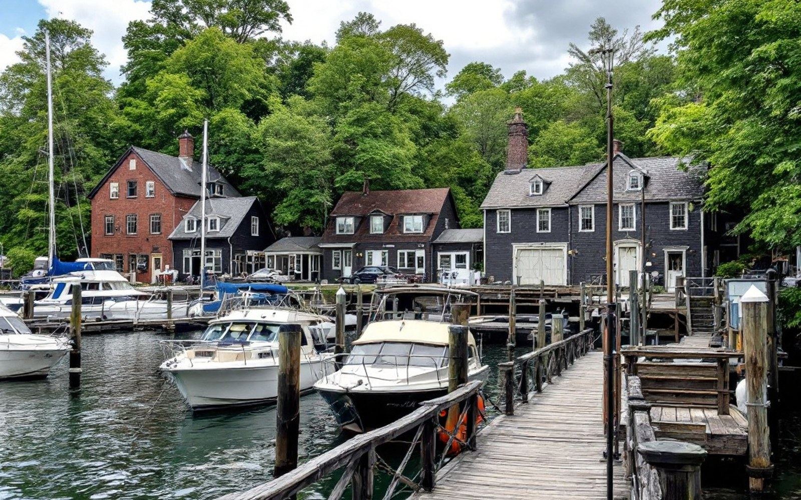 A small dock with boats moored, cottages behind trees