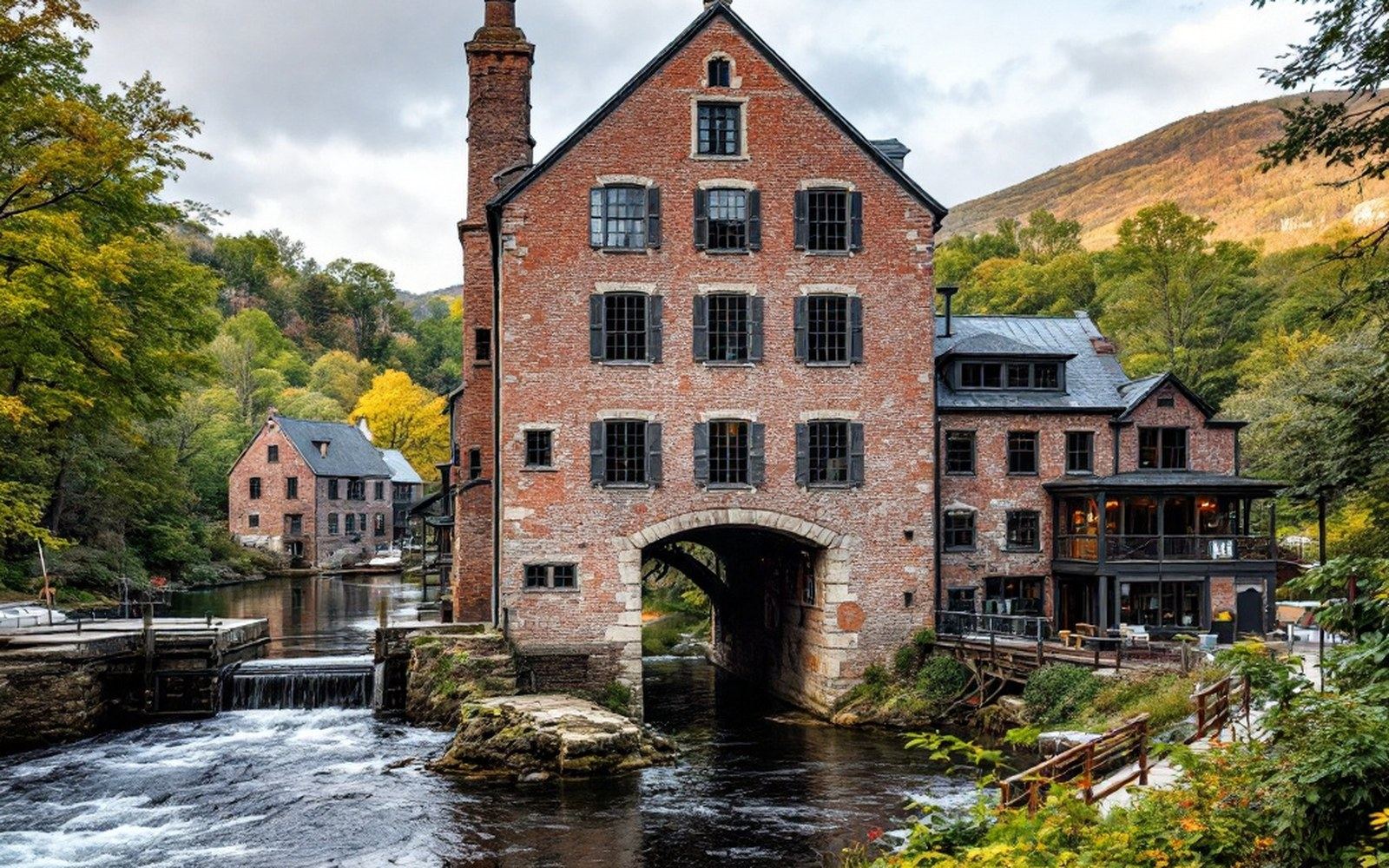 A brick mill building standing above a channel of moving water